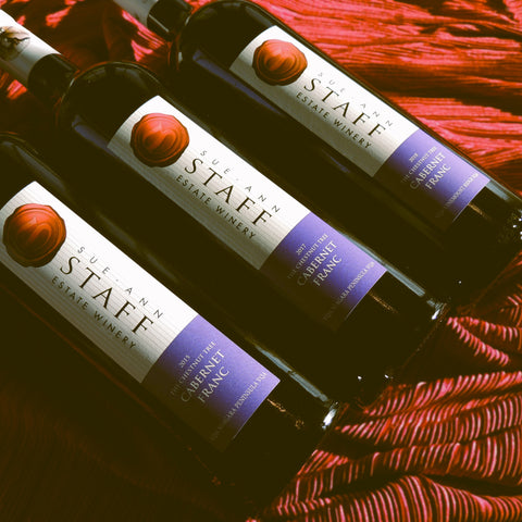 Three bottles of Sue Ann Staff Estate Winery Cabernet Franc on a red textured surface