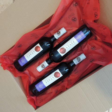 Three bottles of wine with labels on a red tissue paper inside a cardboard box.