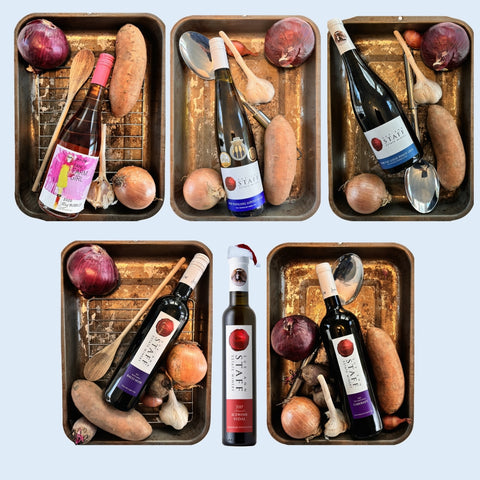 Five metal trays with wine bottles, vegetables, and kitchen utensils on a light blue background