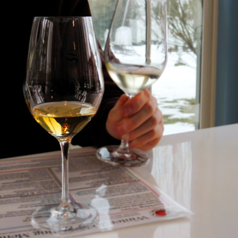 Two wine glasses with one being held by a hand on a newspaper surface.
