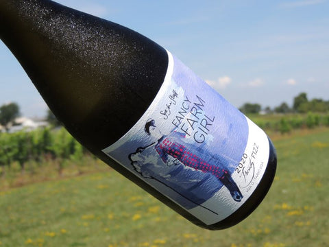 A chilled bottle of Fancy Farm Girl Frosty Fizz photographed in front of the vineyard